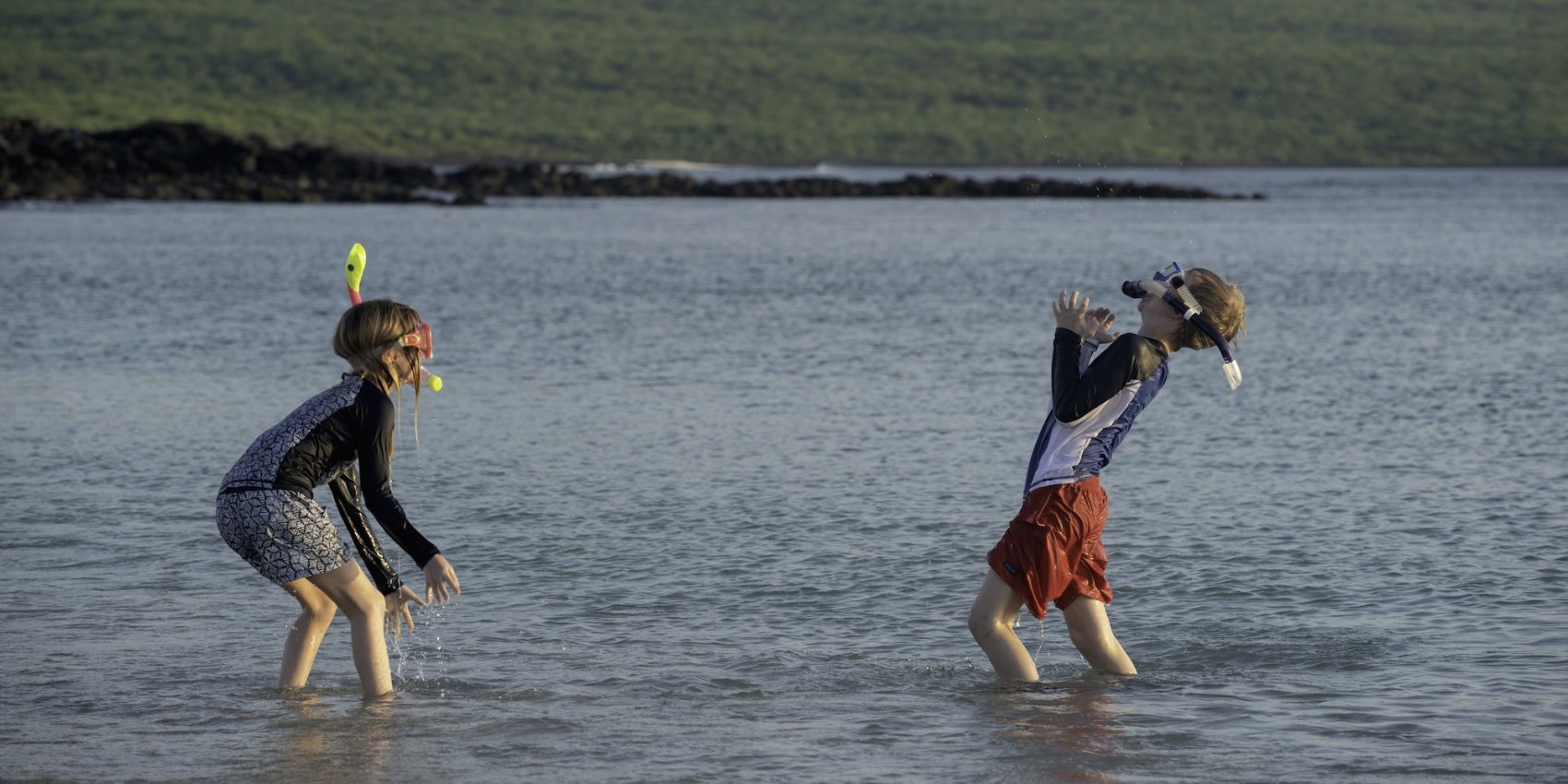 Two kids splashing in shallow ocean water in the Galapagos Islands.
