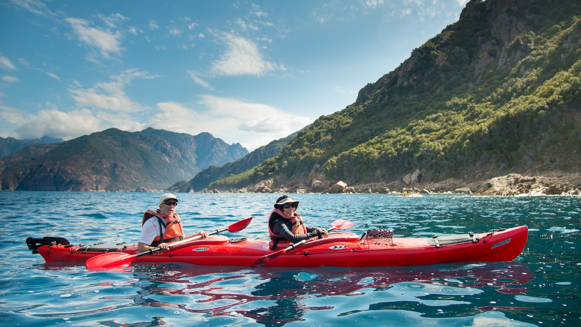 Two people kayaking in a sea kayak off of the shores of Corsica, France.