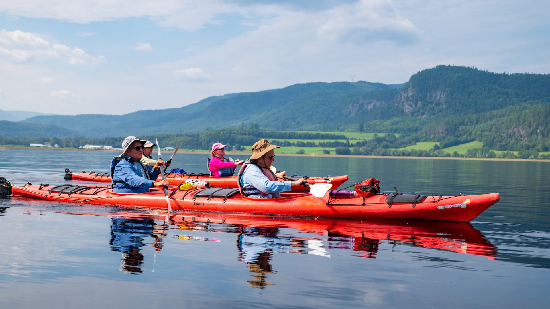 A red tandem sea kayak with sea kayakers paddling atop still water in Quebec