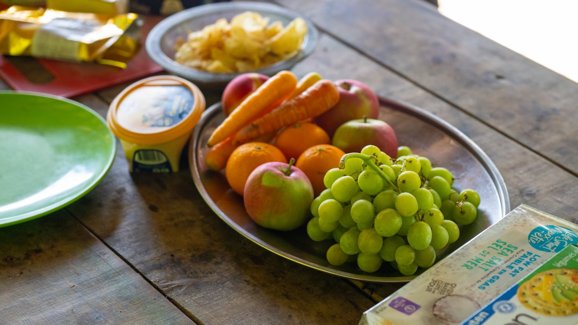 A spread of fruit and crackers on a wooden picnic table 