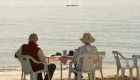 A couple sitting at a camping table enjoying their morning coffee as a whale breaches the surface of the water they are overlooking