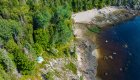 Birds eye view of sea kayaks on shore with a tent set up on a wooden platform amongst a dense forest 