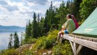 A couple sitting on a wooden platform next to a set up tent overlooking the Saguenay Fjord, Quebec