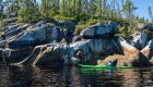 A single kayaker in a green kayak paddling past rock features in Quebec