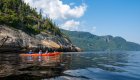 A single kayaker and tandem sea kayak paddling in the sunshine close to a rocky shore